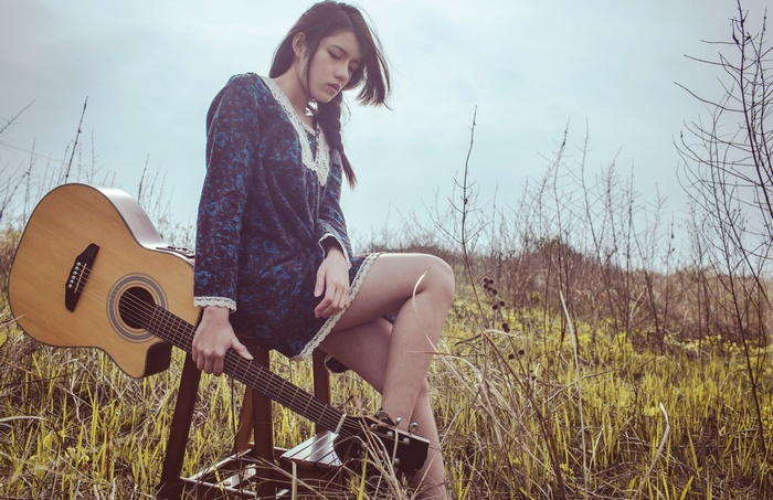Asian woman with guitar sitting outdoors