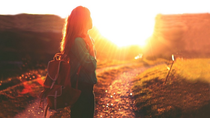 Woman with backpack on dirt road during golden hour