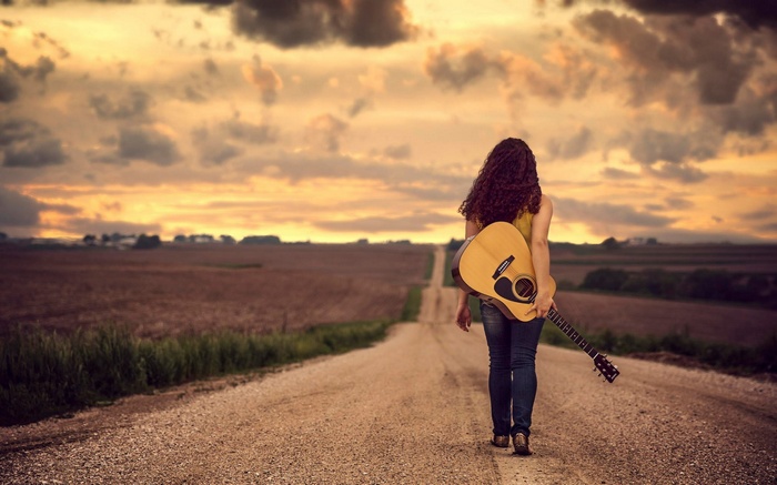 Woman with guitar walking on a dirt road in Nebraska