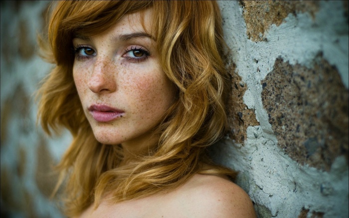 Vica Kerekes with freckles leaning against a stone wall