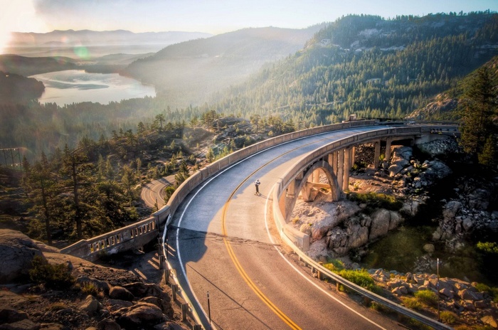 Person longboarding on a scenic bridge over a forest and lake