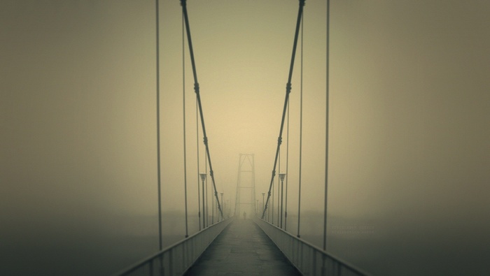 A lone figure walks across a foggy suspension bridge