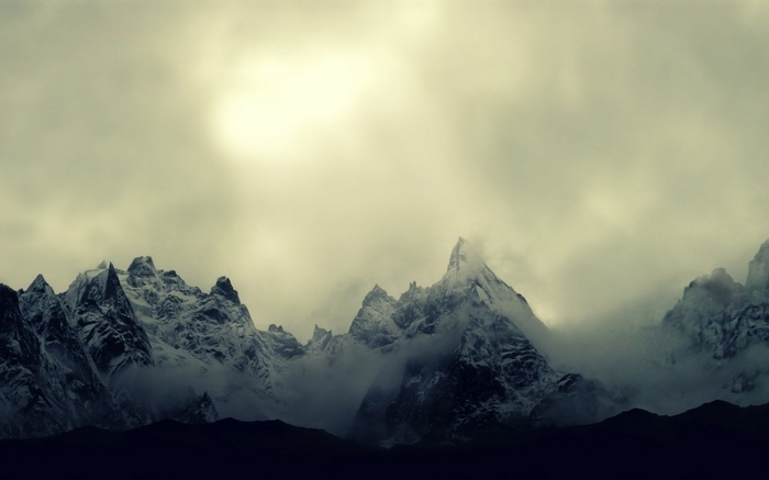 Snow-capped mountains shrouded in mist under a bright sky