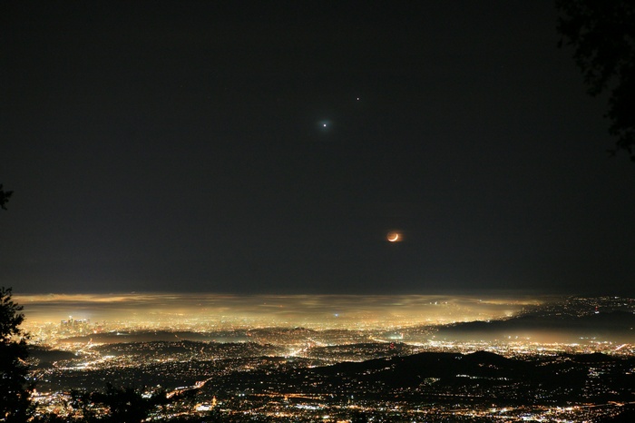 Cityscape at night with Venus, Jupiter, and a lunar eclipse