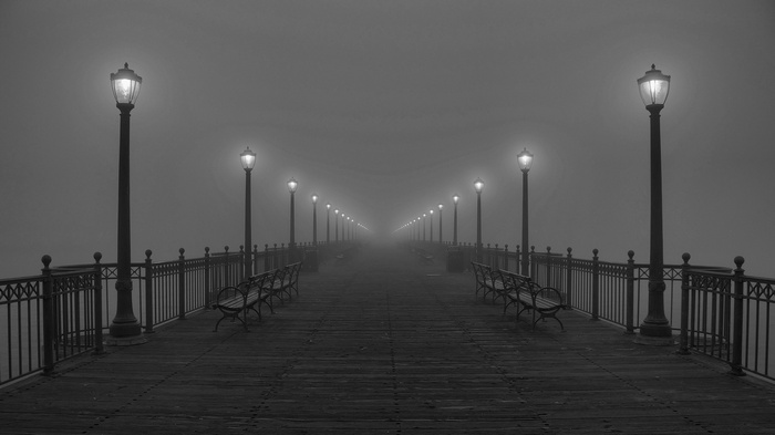 A foggy pier with lanterns and benches