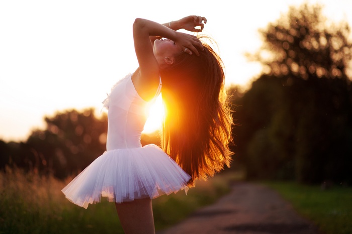 Ballerina with hands on head in sunlight outdoors