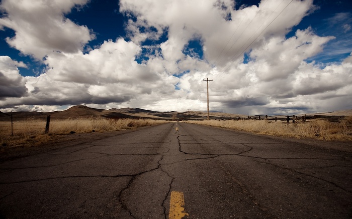 Cracked asphalt road through a dry landscape under cloudy sky