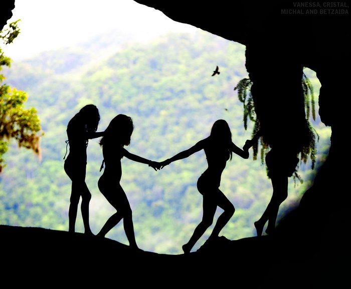 Four women holding hands in a cave entrance