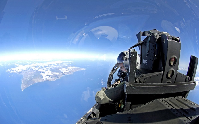 Pilot in a jet fighter cockpit overlooking an island