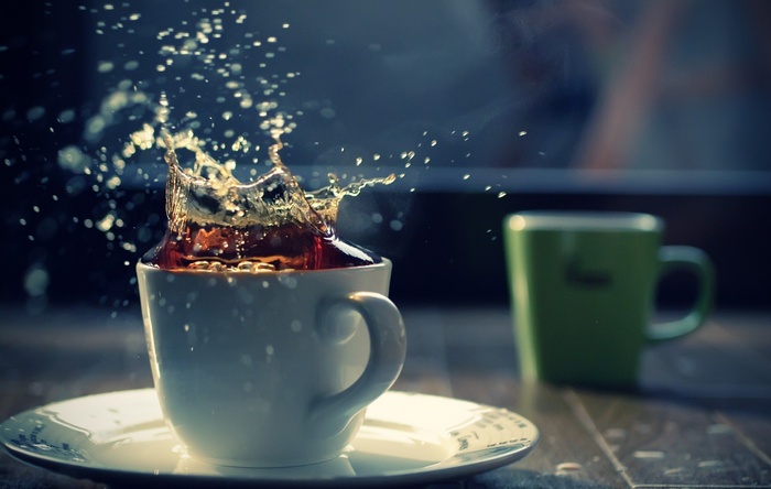 Tea splashing in a white cup with a green cup in the background