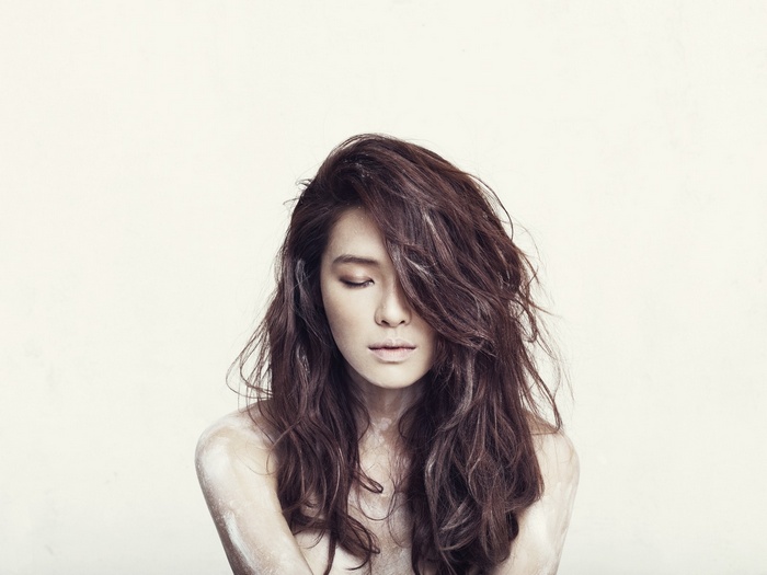 Kahi with long wavy brown hair and closed eyes