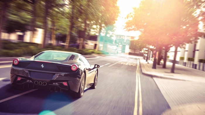 Black Ferrari driving on a street with trees