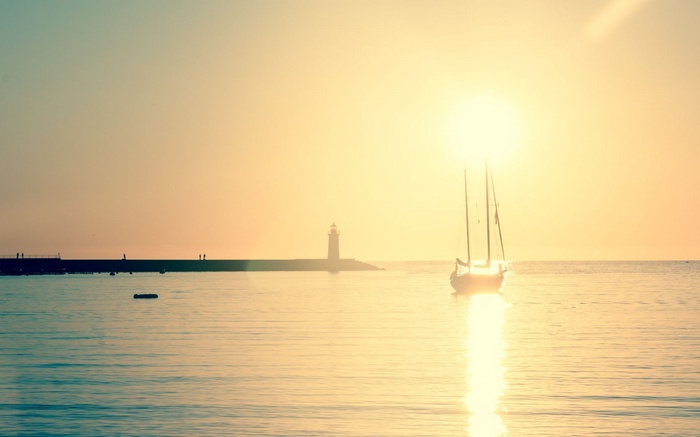 Sailboat and lighthouse at sunset over the sea