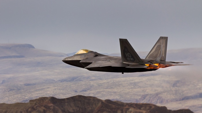 F-22 Raptor flying over desert mountains