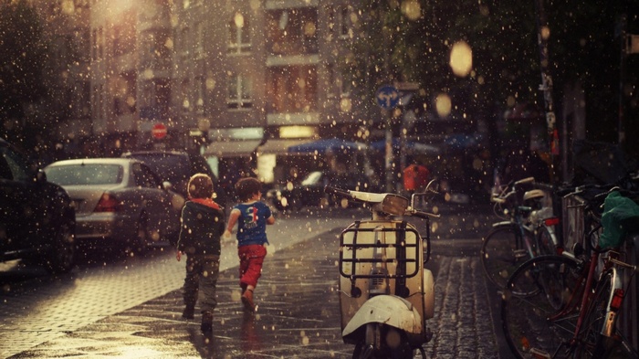 Two children run in the rain on a city street