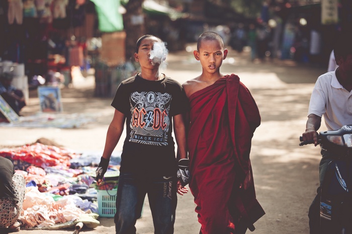 Two young boys, one smoking, one a monk, walk in a market