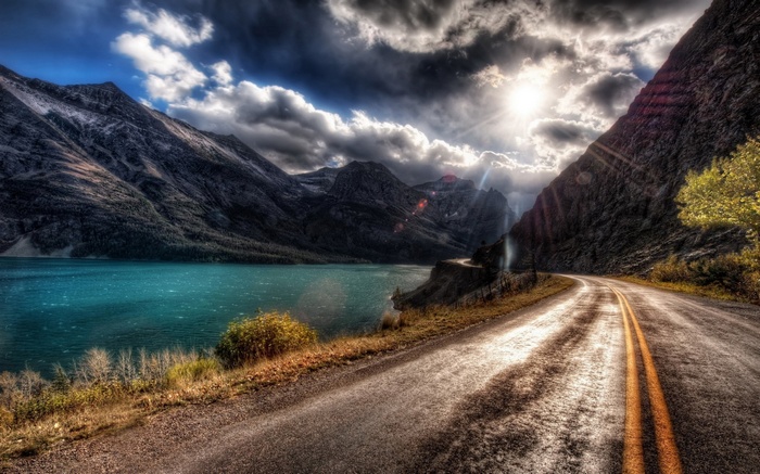 Road by a turquoise lake and mountains under a dramatic sky