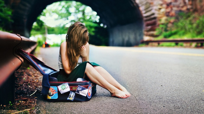 Woman sitting by a suitcase on the side of the road