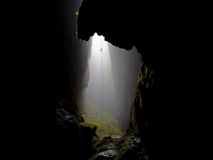 Spelunker rappelling down into a misty cave opening