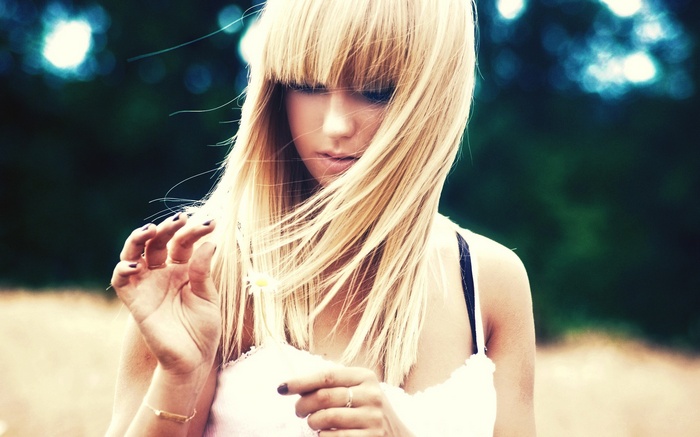 Woman with blonde hair holding a flower outdoors