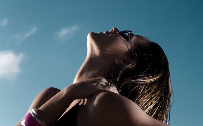 Woman wearing sunglasses and bracelets against blue sky