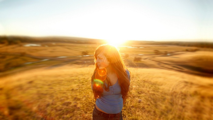 Woman with long hair in a field at sunset with lens flare