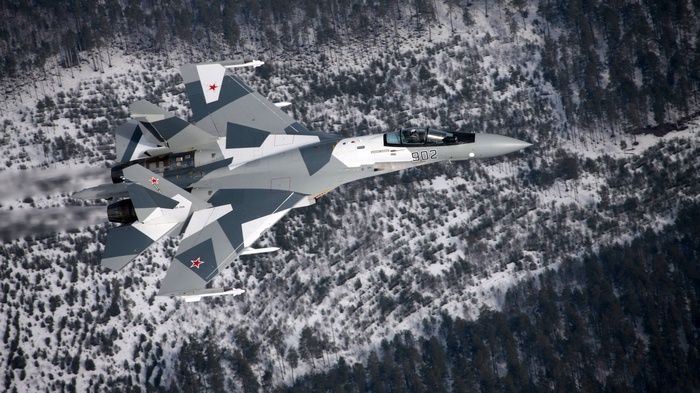 Russian Su-27 fighter jet flying over a snowy forest
