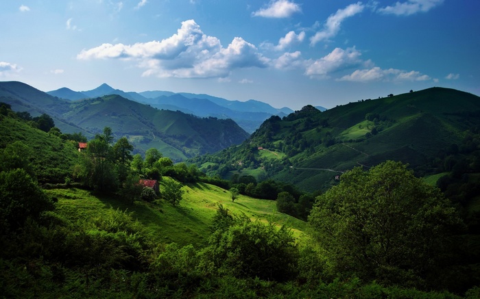 Green mountains and valleys under a blue sky with clouds