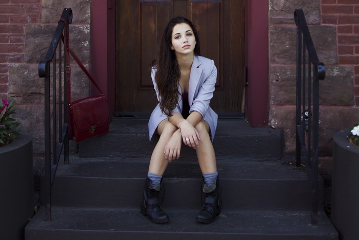 Emily Rudd sitting on steps with a red purse
