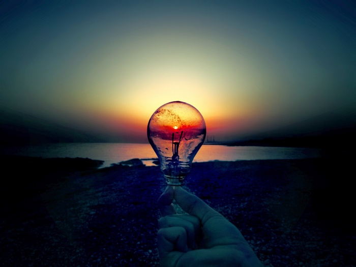 Light bulb held against a sunset over the ocean