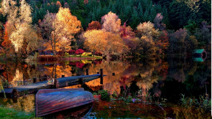 Autumn trees reflected in a calm lake with a boat and dock