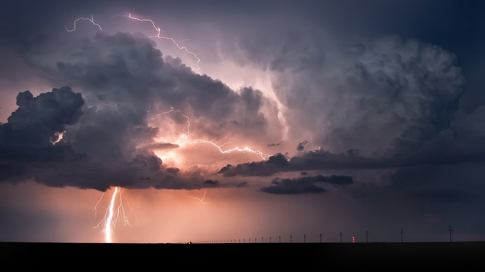 Lightning strikes through dark storm clouds over a flat landscape.