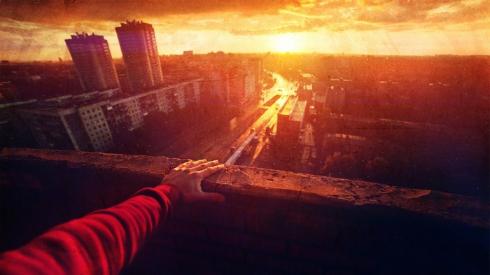 Hand on ledge overlooking city at sunset
