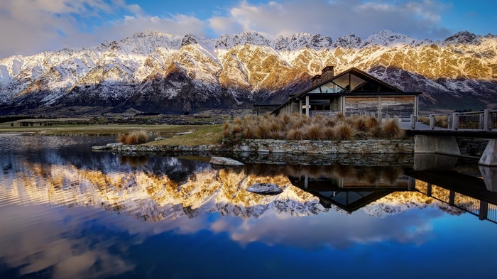 Snow-capped mountains reflected in a lake near a modern house