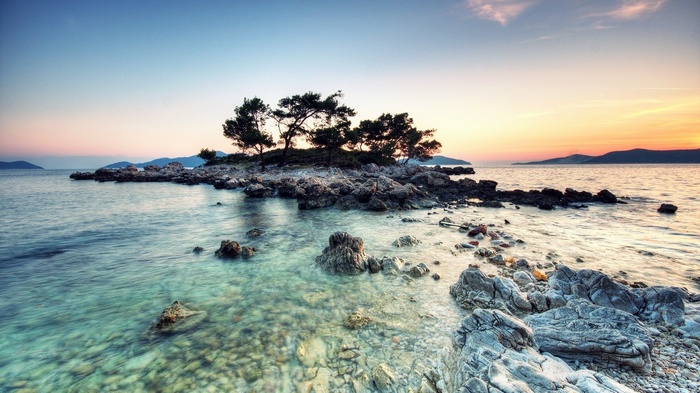 Rocky island with trees in the sea at sunset