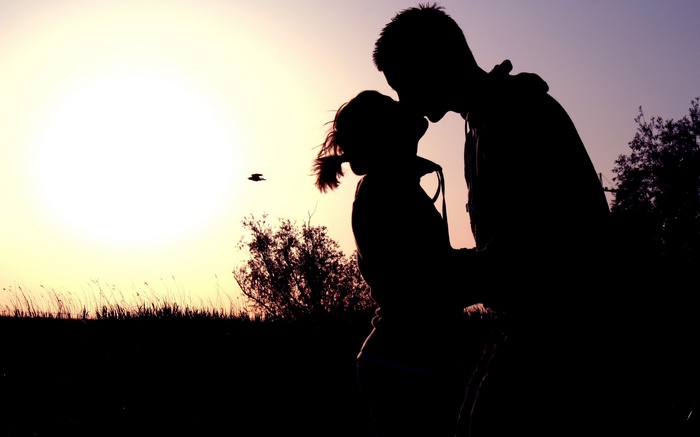 Couple kissing at sunset with a bird flying