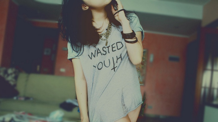 Woman wearing a grey t-shirt with 'Wasted Youth' text