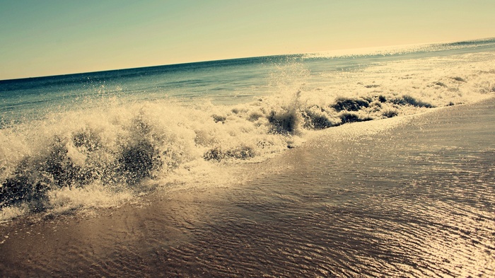 Ocean waves crashing on a sandy beach at sunset