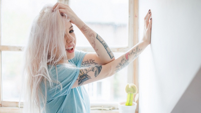 Woman with blonde hair and tattoos by the window