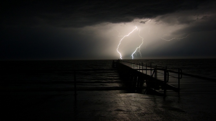 Lightning strikes over a pier at night