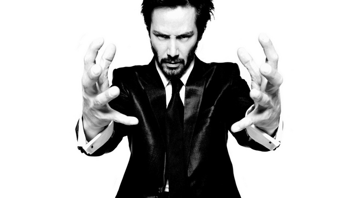 Keanu Reeves in a black suit with hands outstretched