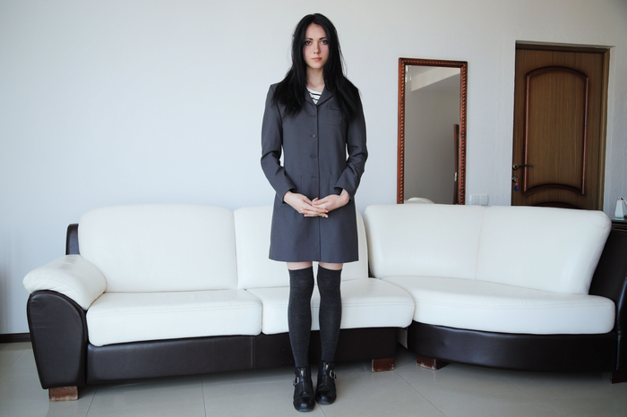 Woman in a gray coat and knee-highs standing by a couch