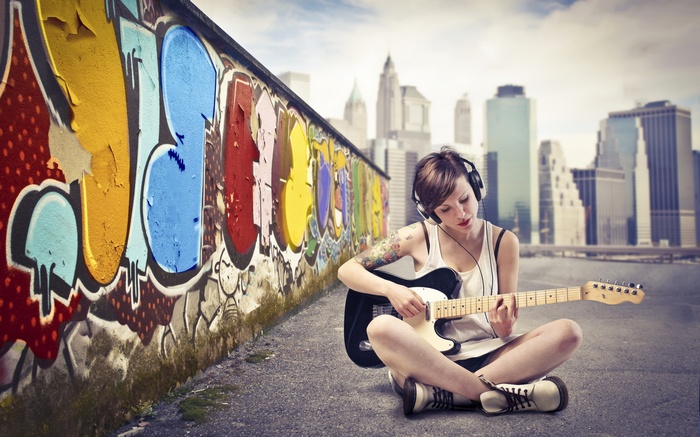 Woman playing guitar near graffiti wall with cityscape