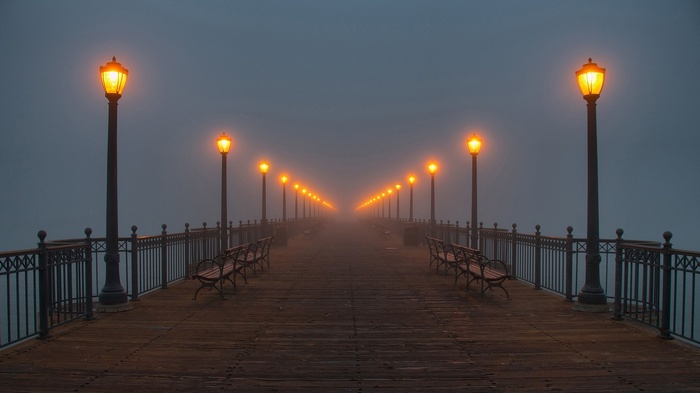Pier with lanterns in the mist at night