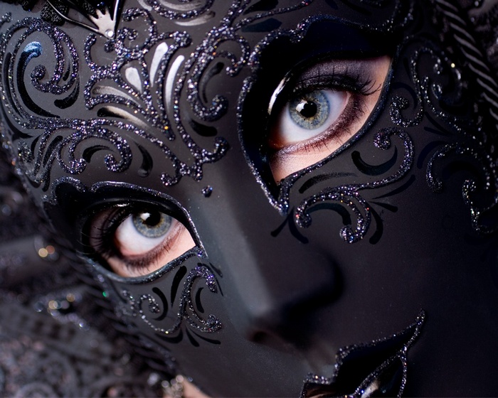 Woman wearing a black Venetian mask with blue eyes