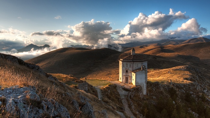 Chapel on a hill with mountains and clouds