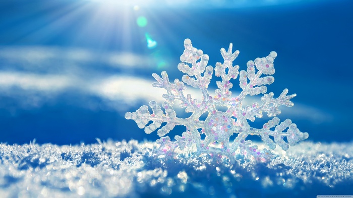 Close-up of a snowflake on snow with sun rays
