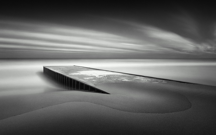 Monochrome long exposure of a pier on a sandy beach