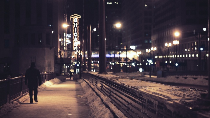 Man walks on a snowy sidewalk in Chicago at night