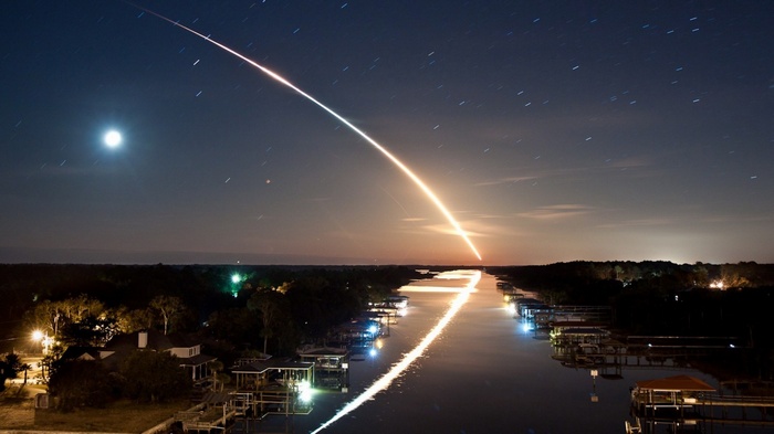 Rocket Launch Over River at Night with Moon and Stars